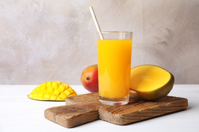 Photo of Glass with fresh mango juice and tasty fruits on table. Space for text