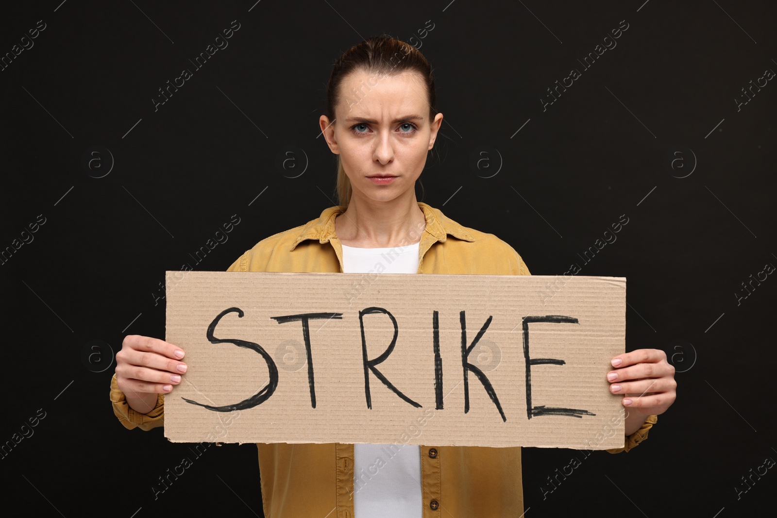 Photo of Angry woman holding cardboard banner with word Strike on black background