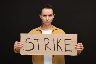 Photo of Angry woman holding cardboard banner with word Strike on black background