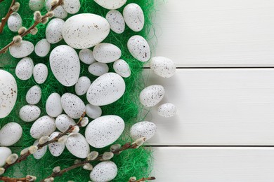 Photo of Many beautifully painted Easter eggs and pussy willow branches on white wooden table, flat lay. Space for text