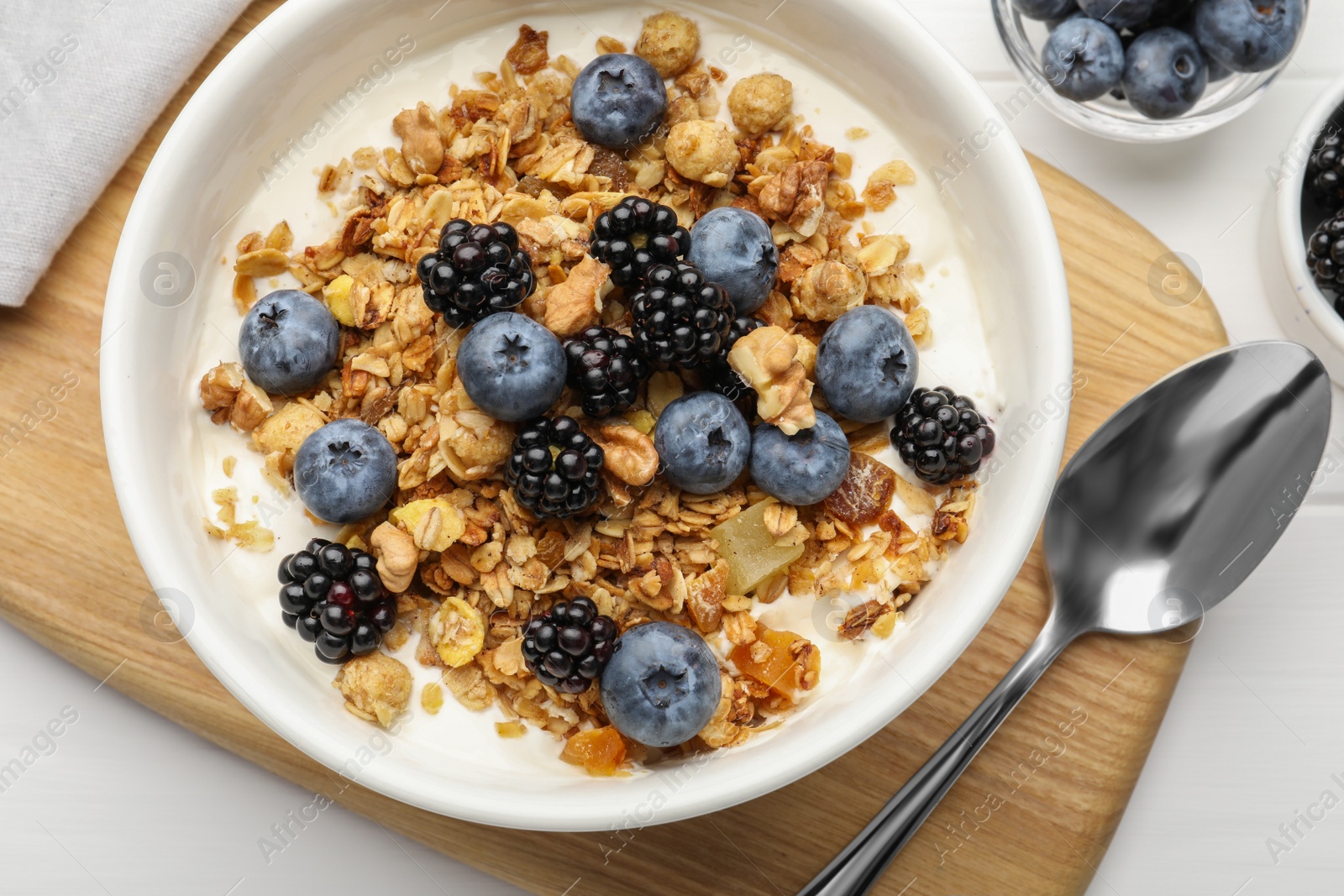 Photo of Bowl of healthy muesli served with berries on white wooden table, flat lay