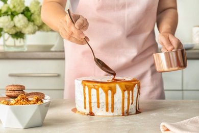 Young woman applying caramel sauce onto delicious homemade cake at table