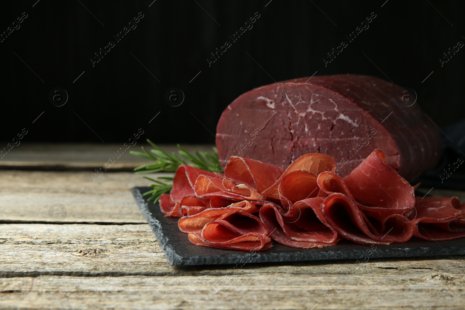 Photo of Tasty bresaola and rosemary on wooden table, closeup. Space for text