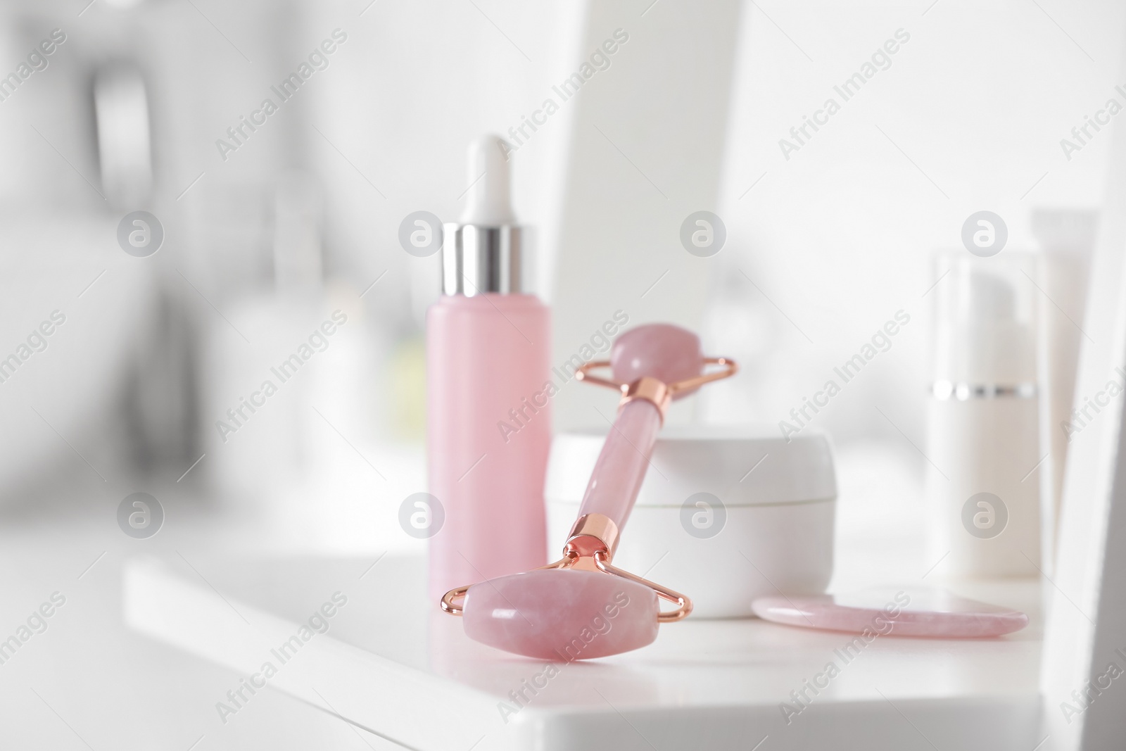 Photo of Natural face roller, gua sha tool and cosmetic products on shelving unit in bathroom, closeup. Space for text