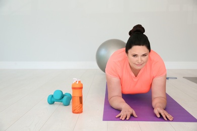 Overweight woman doing plank exercise on mat in gym