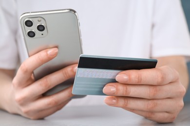 Photo of Online payment. Woman with smartphone and credit card at white table, closeup