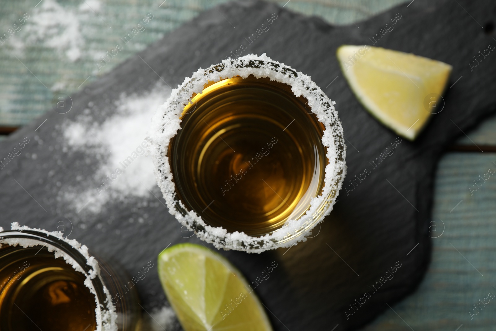 Photo of Mexican Tequila shots, lime slices and salt on blue wooden table, top view