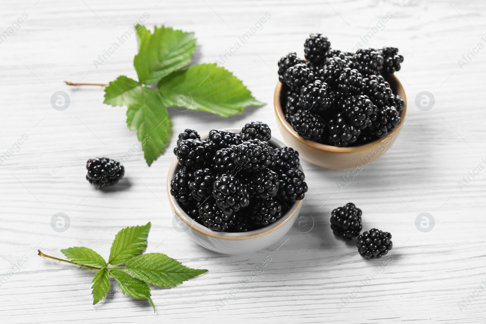 Photo of Ripe blackberries and green leaves on white wooden table