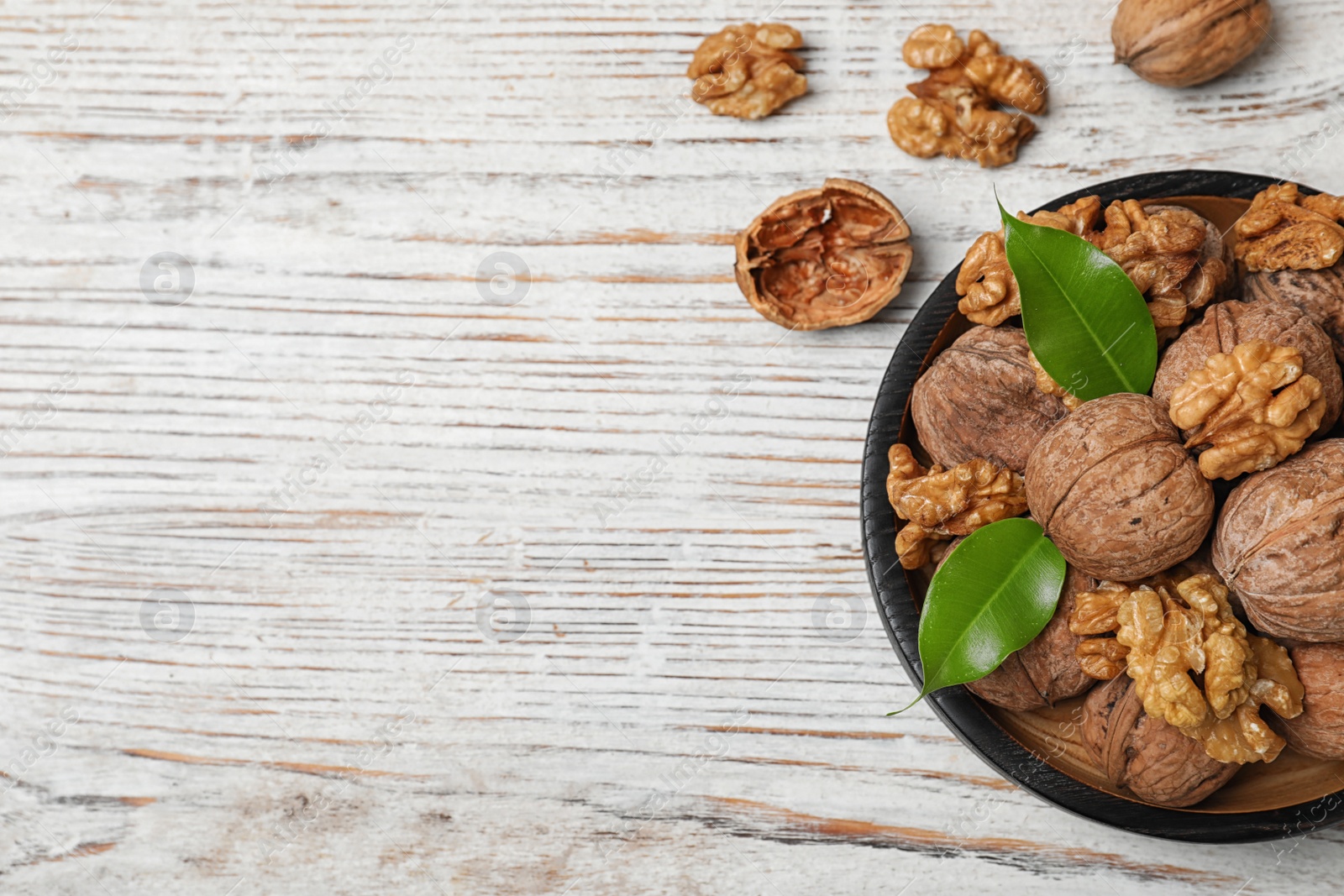 Photo of Plate with walnuts and space for text on wooden background, top view