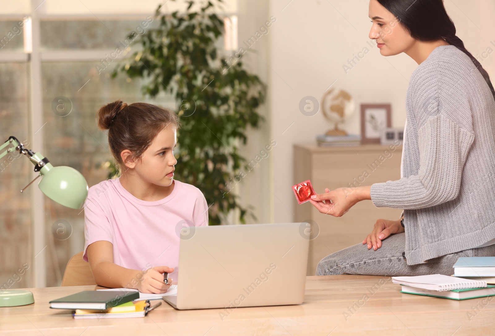 Photo of Mother talking with her teenage daughter about contraception while she doing homework at home. Sex education concept