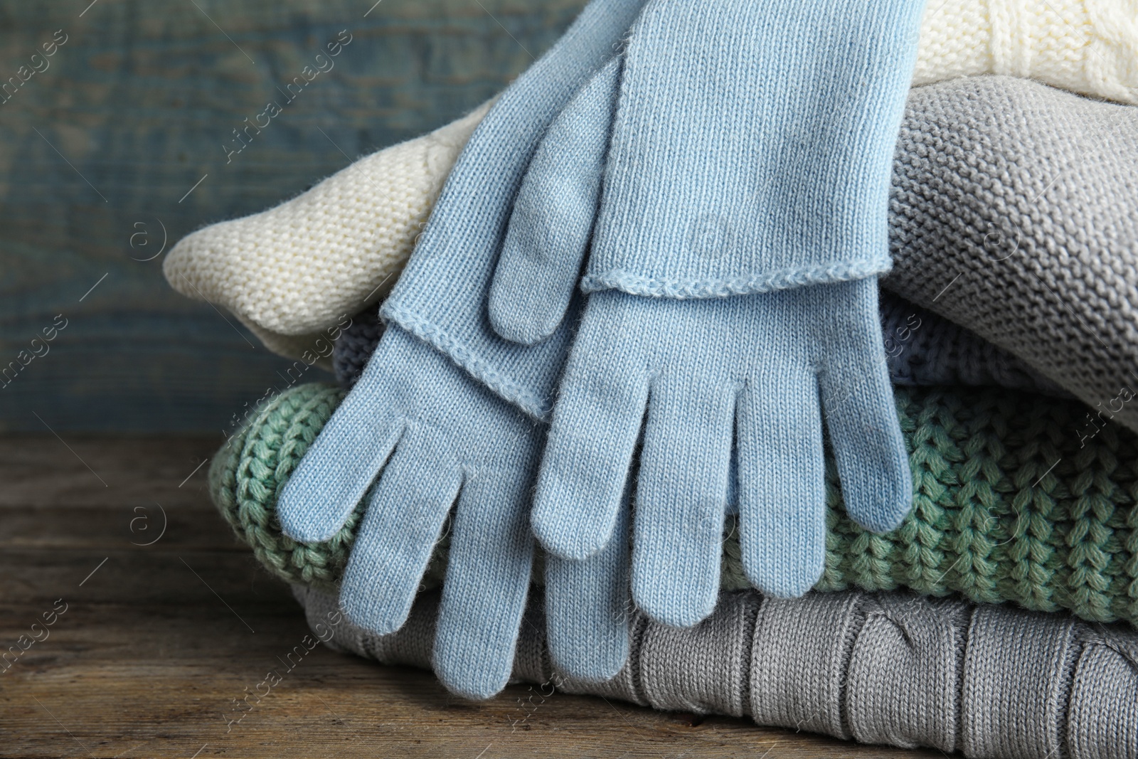 Photo of Stacked sweaters and gloves on wooden table, closeup. Autumn clothes