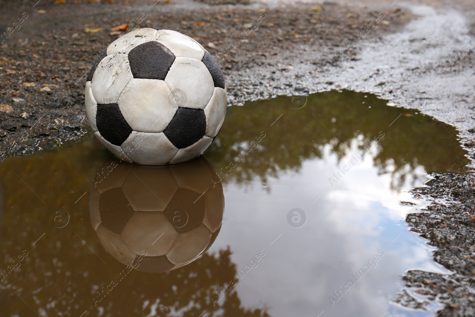 Photo of Dirty soccer ball in muddy puddle, space for text