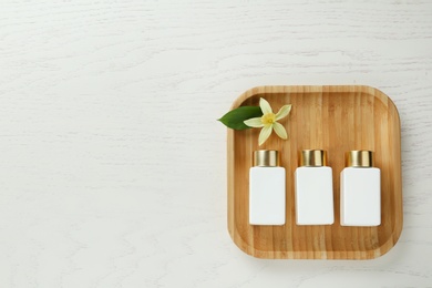 Top view of wooden tray with cosmetic bottles and flower on white table, space for text. Spa treatment