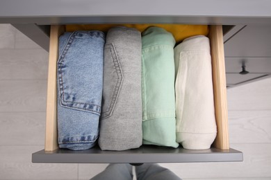 Photo of Woman near open drawer with folded clothes indoors, top view. Vertical storage