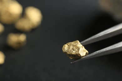 Tweezer with shiny gold nugget on blurred background, closeup. Space for text