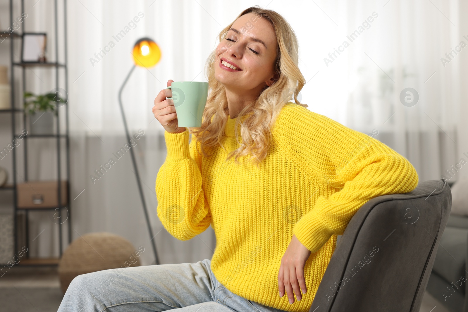 Photo of Happy woman in stylish warm sweater holding cup of drink at home