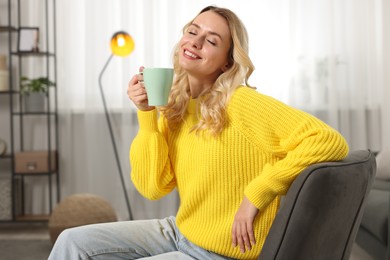 Happy woman in stylish warm sweater holding cup of drink at home