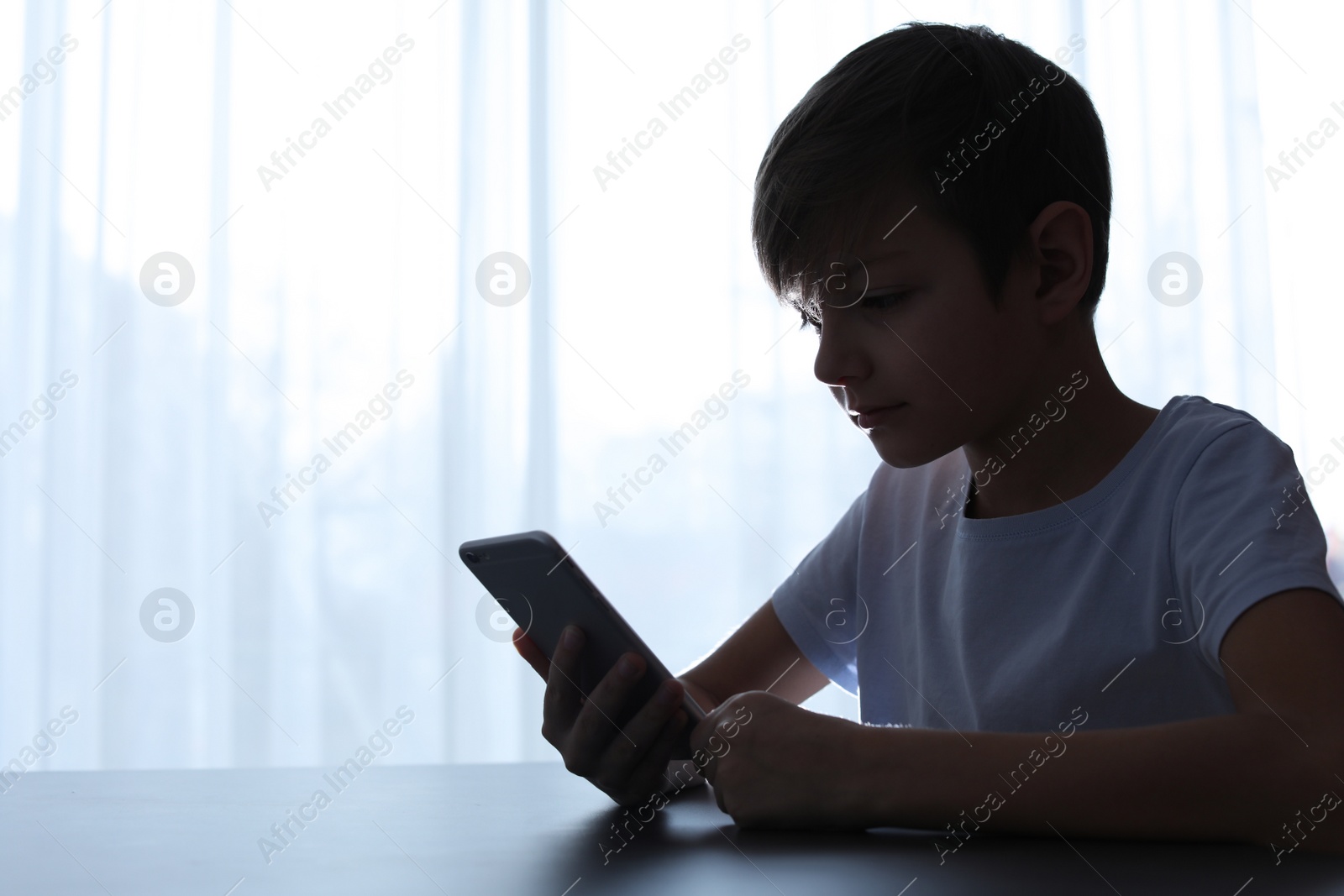 Photo of Child with smartphone at table indoors. Danger of internet