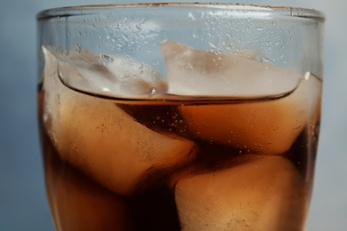 Photo of Glass of refreshing soda drink with ice cubes on blue background, closeup