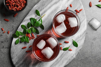 Photo of Healthy goji juice in glasses served on grey table, flat lay