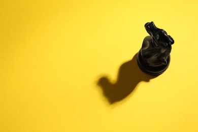 Photo of Black wooden chess knight on yellow background, above view. Space for text