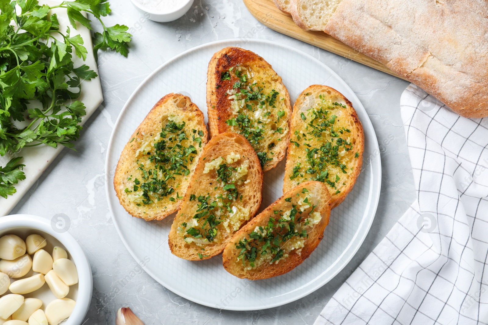 Photo of Slices of toasted bread with garlic and herb on light grey marble table, flat lay