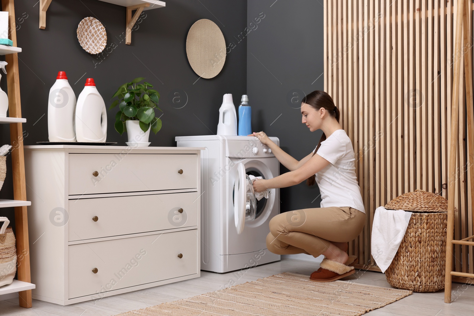 Photo of Beautiful woman putting shirt into washing machine in laundry room