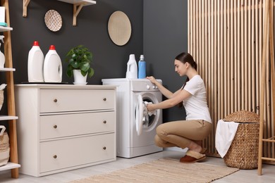 Beautiful woman putting shirt into washing machine in laundry room