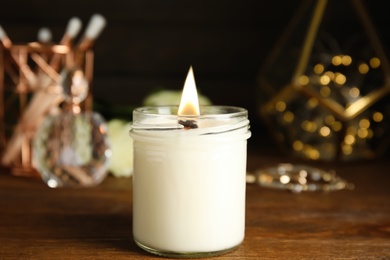 Burning candle and jewelry on wooden table