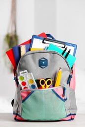 Backpack with different school stationery on white table indoors