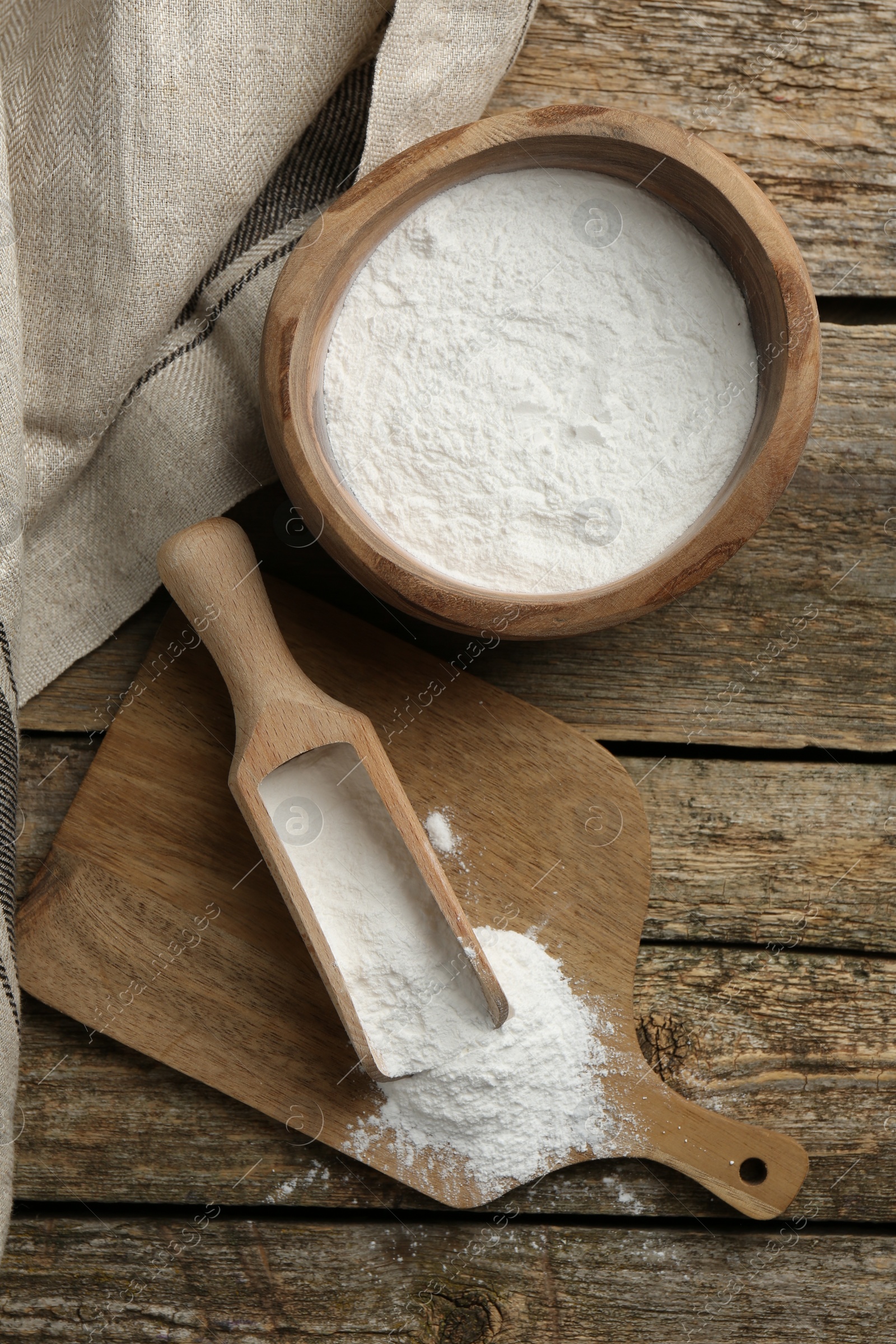 Photo of Baking powder in bowl and scoop on wooden table, flat lay