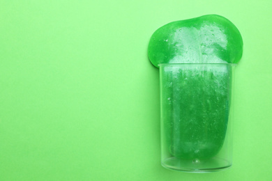 Overturned plastic container with bright slime on green background, top view. Space for text