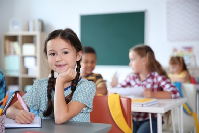 Photo of Cute little child sitting at desk in classroom. Elementary school