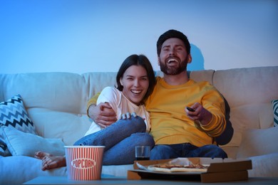 Photo of Happy couple watching TV with popcorn and pizza on sofa