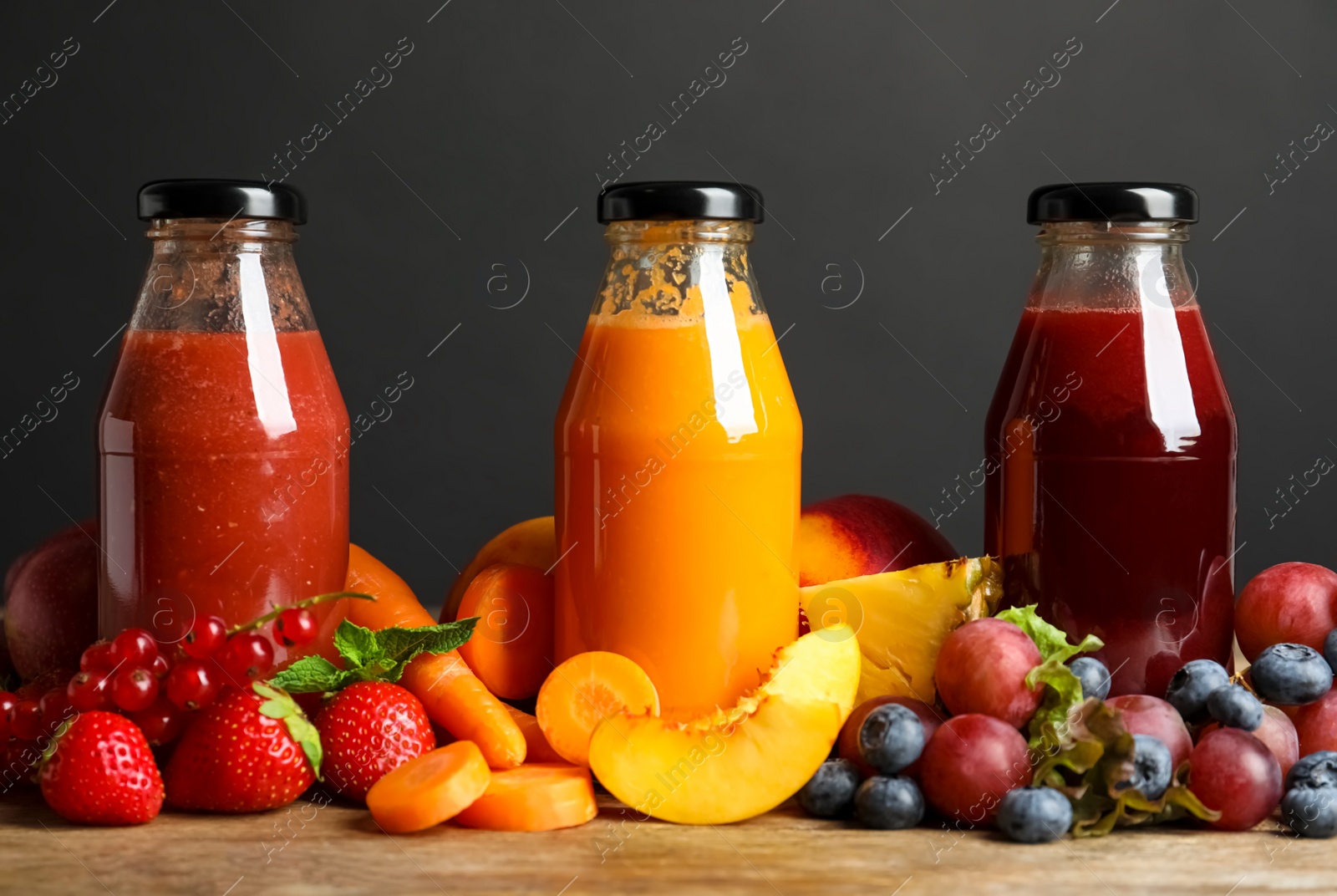 Photo of Bottles of delicious juices and fresh fruits on wooden table