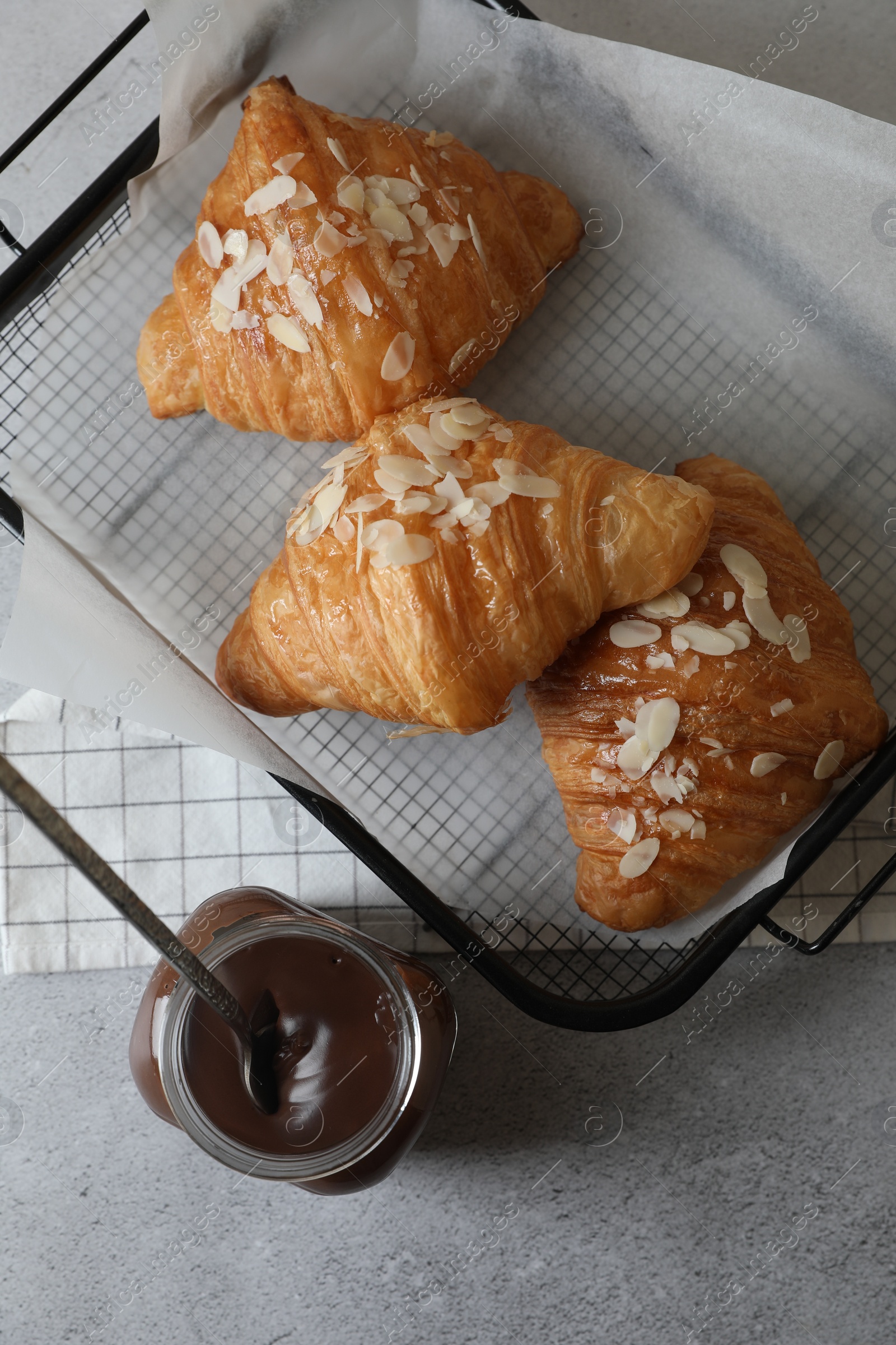 Photo of Delicious croissants with almond flakes and chocolate paste on light grey table, flat lay