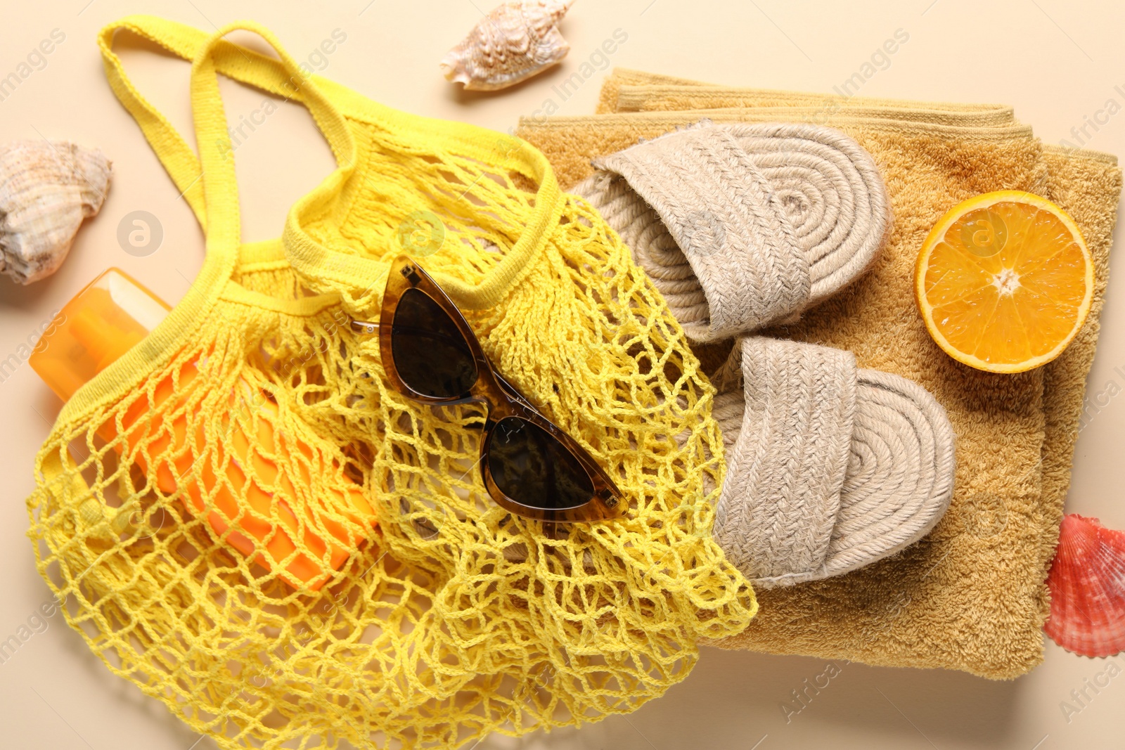 Photo of String bag, different beach accessories and orange on beige background, top view