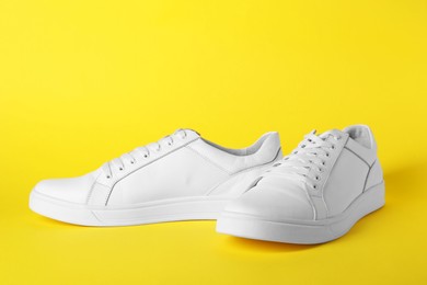 Photo of Pair of stylish white sneakers on yellow background