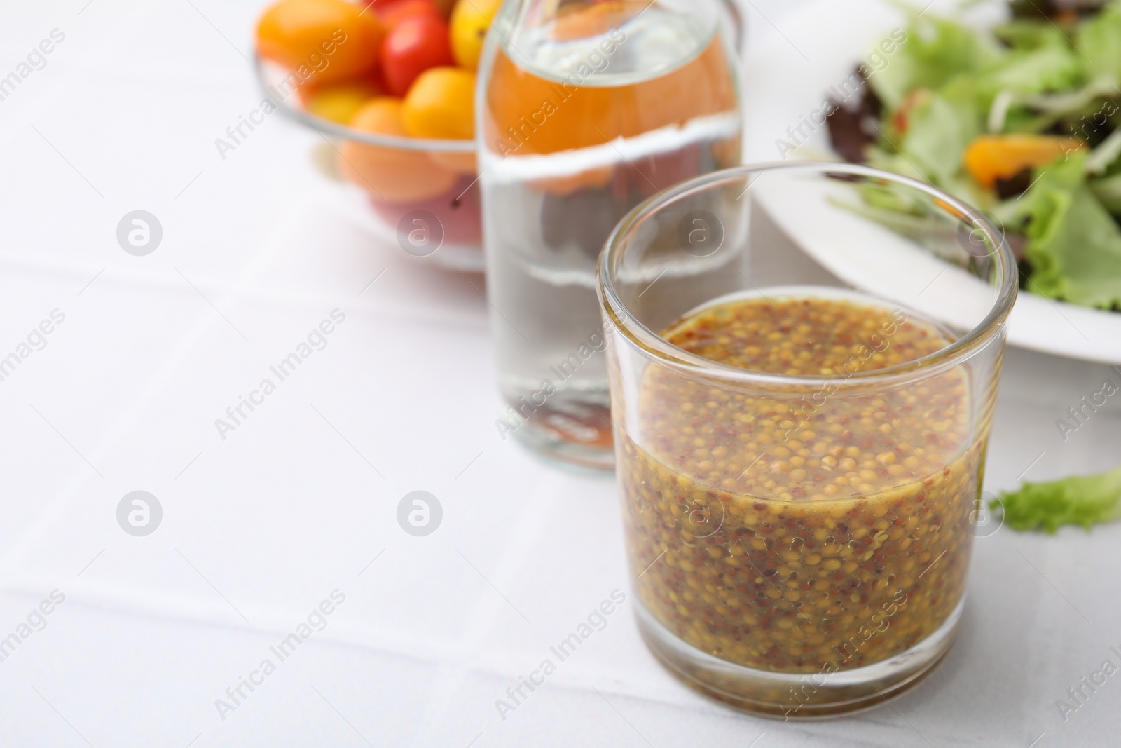 Photo of Tasty vinegar based sauce (Vinaigrette) in glass on light tiled table, closeup. Space for text