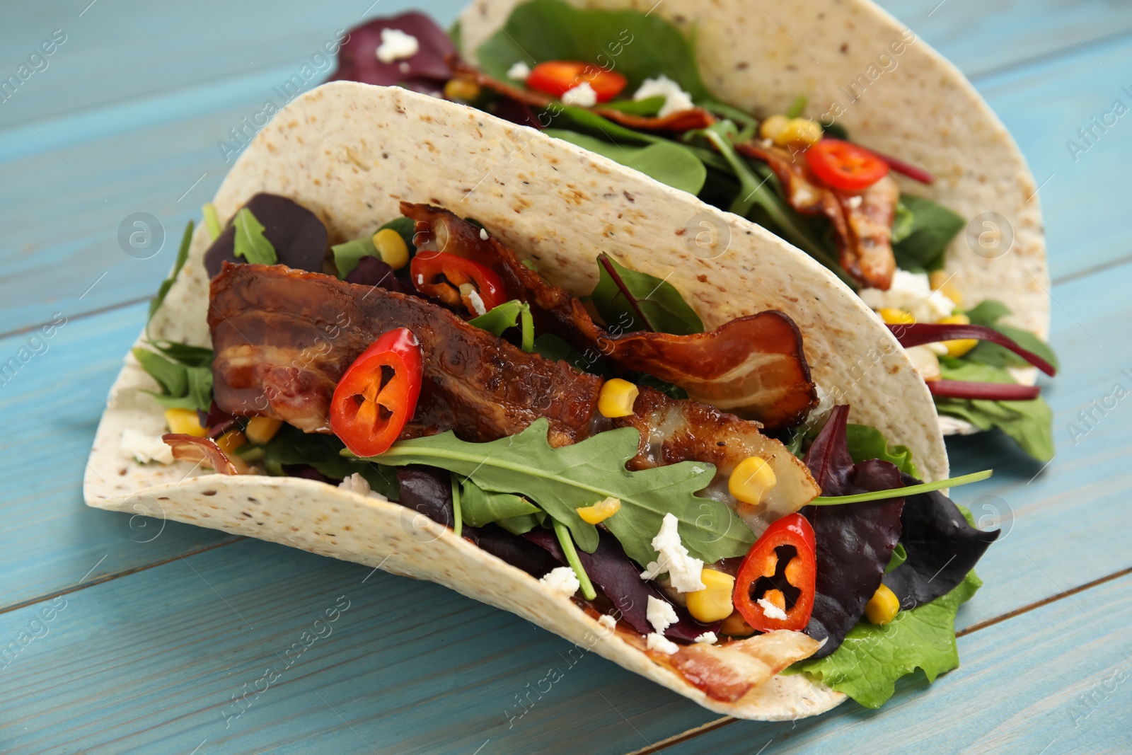 Photo of Delicious tacos with fried bacon, vegetables and cheese on turquoise wooden table, closeup