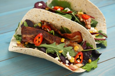 Photo of Delicious tacos with fried bacon, vegetables and cheese on turquoise wooden table, closeup