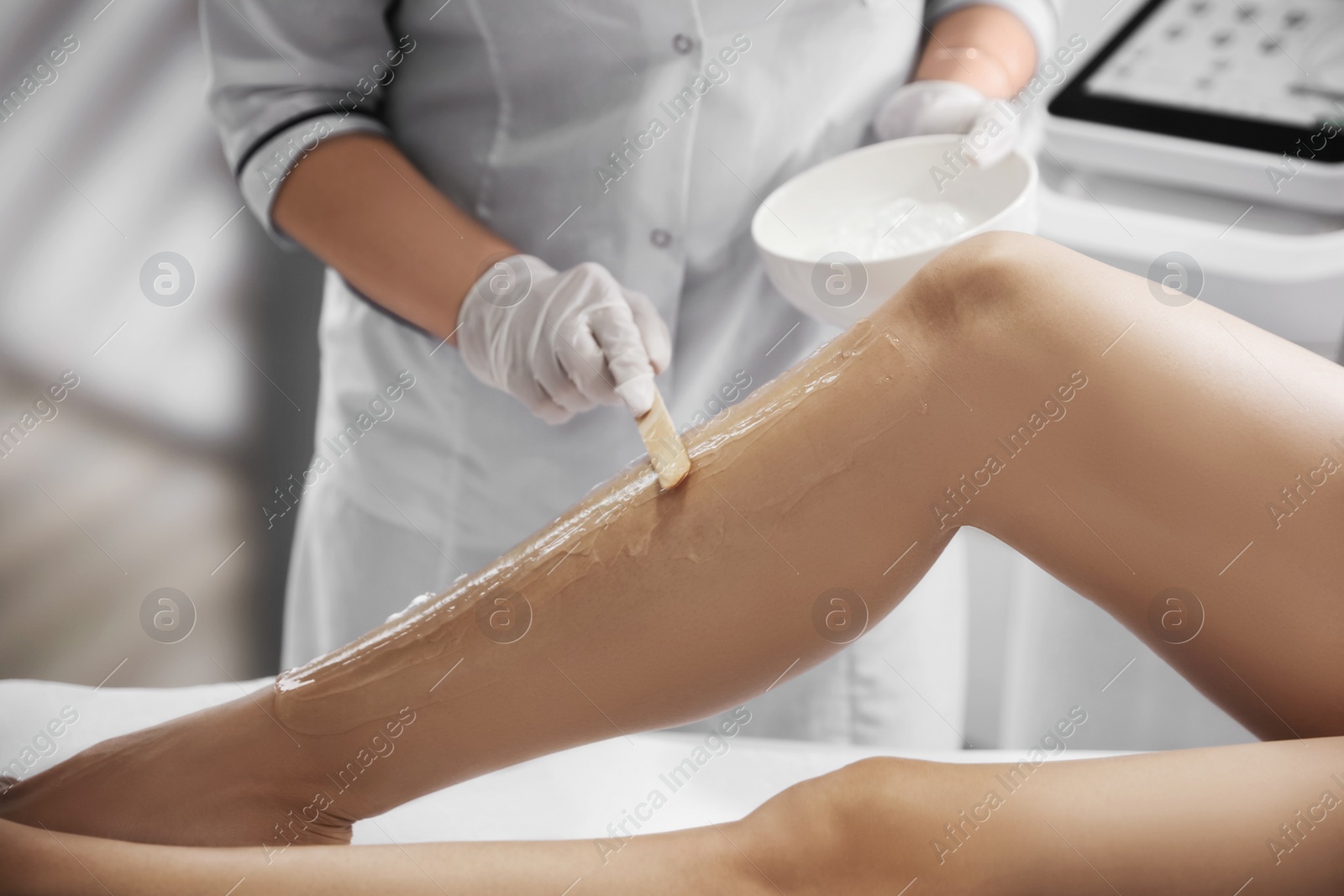 Photo of Professional cosmetologist applying gel on client's leg before laser epilation procedure in salon, closeup