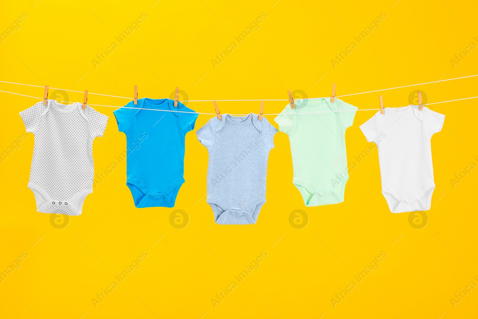 Photo of Baby onesies hanging on clothes line against yellow background