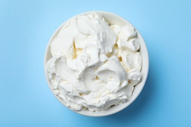 Photo of Bowl of tasty cream cheese on light blue background, top view