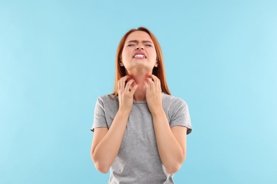 Suffering from allergy. Young woman scratching her neck on light blue background