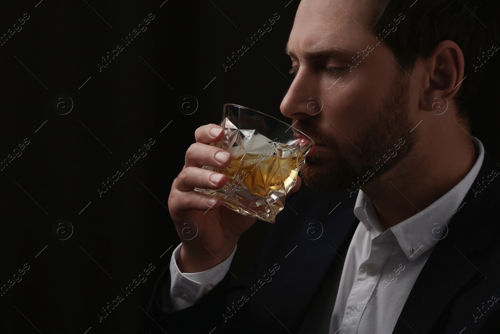 Photo of Man in suit drinking whiskey on black background. Space for text