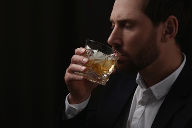 Man in suit drinking whiskey on black background. Space for text