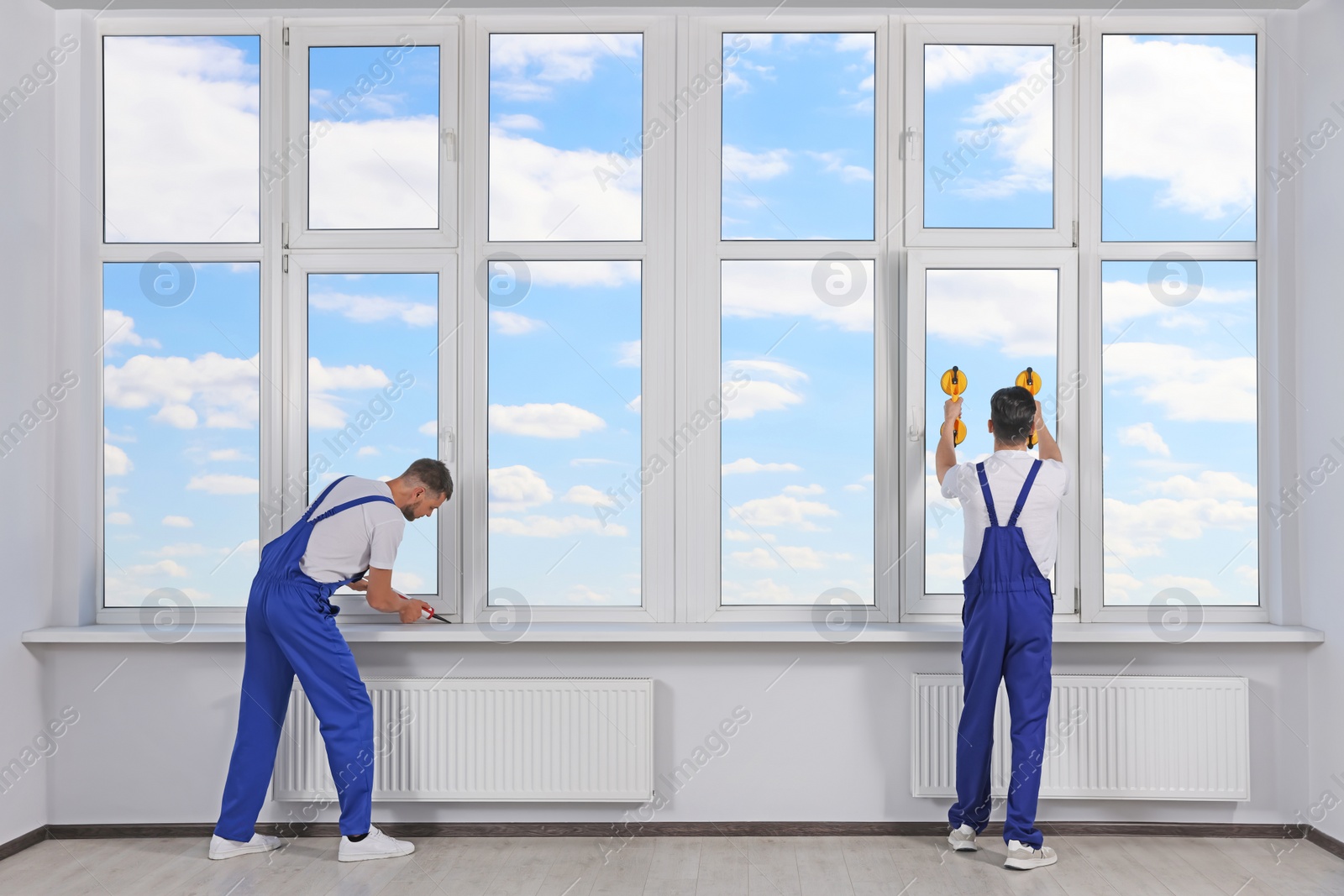 Photo of Workers with tube of sealant and suction lifters installing plastic windows indoors