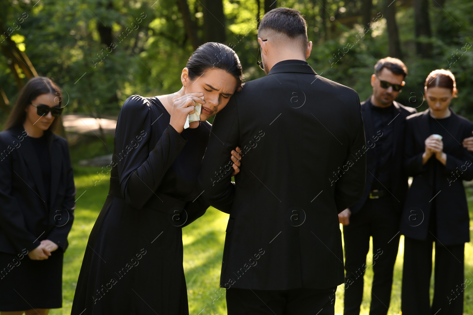 Photo of Sad people in black clothes mourning outdoors. Funeral ceremony