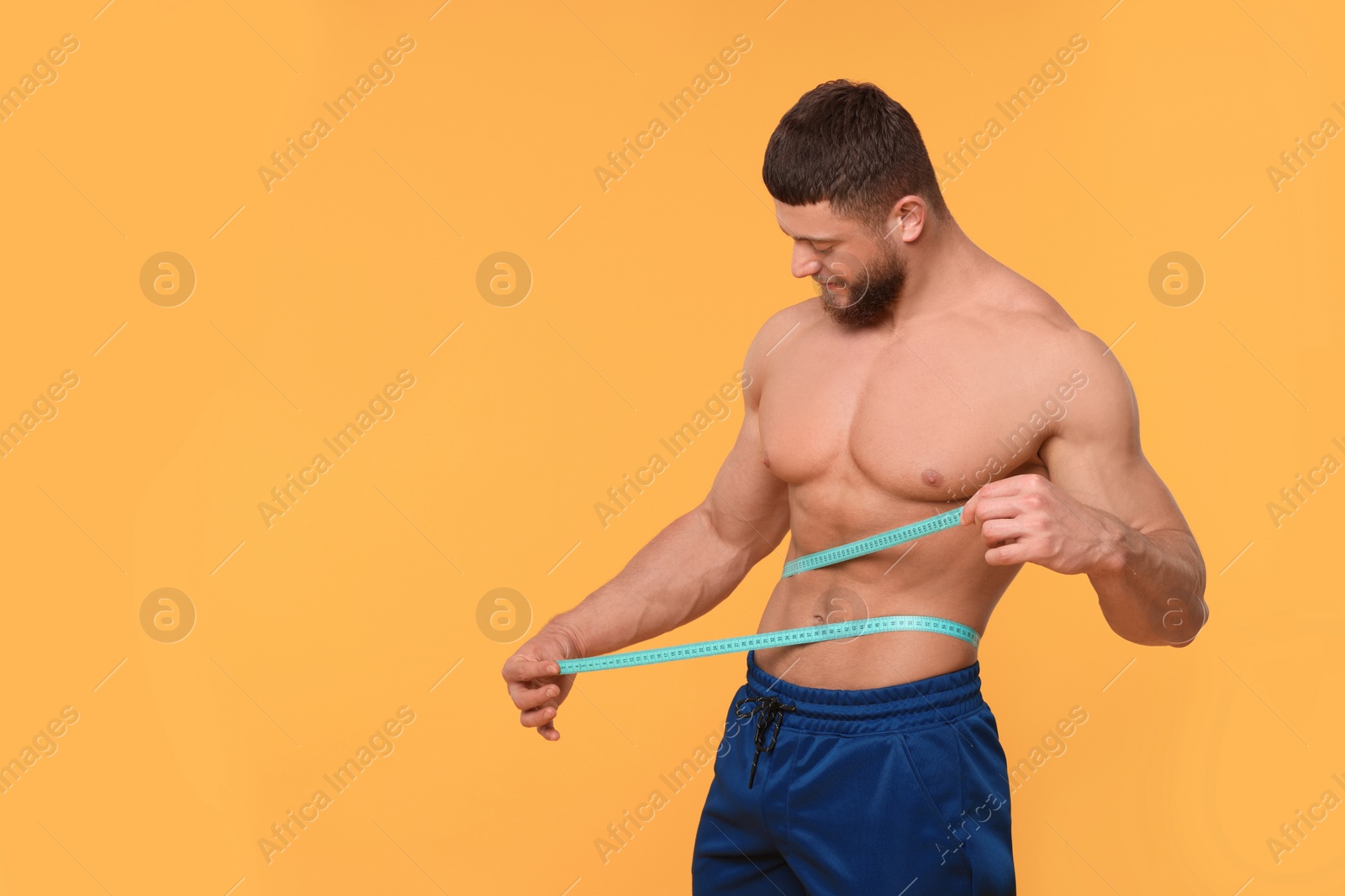 Photo of Athletic man measuring waist with tape on orange background, space for text. Weight loss concept